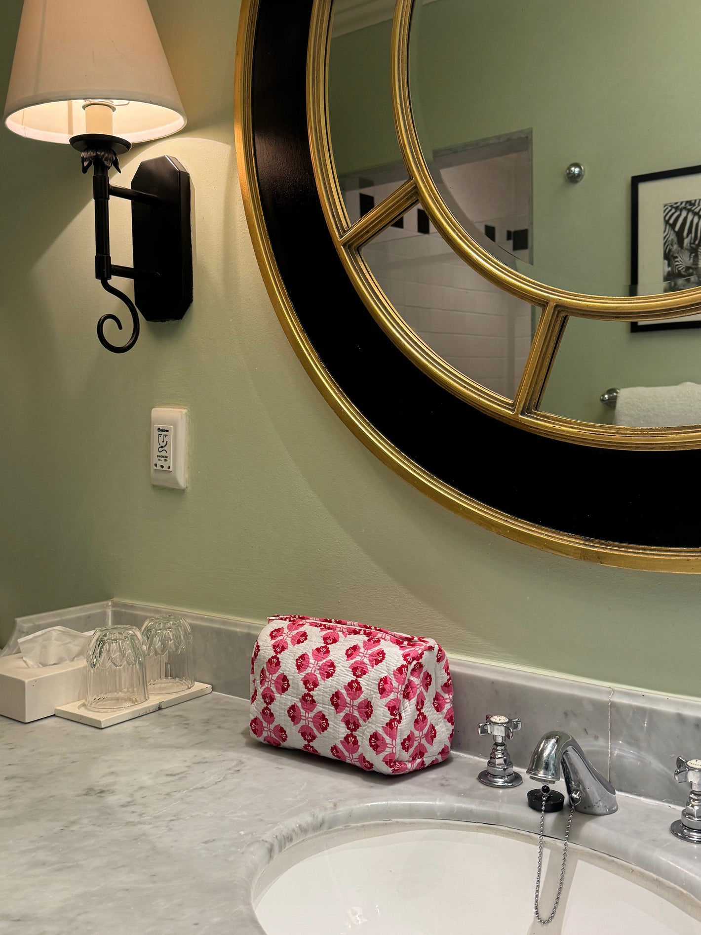 Bathroom vanity with round mirror, pink floral bag, and light fixture.
