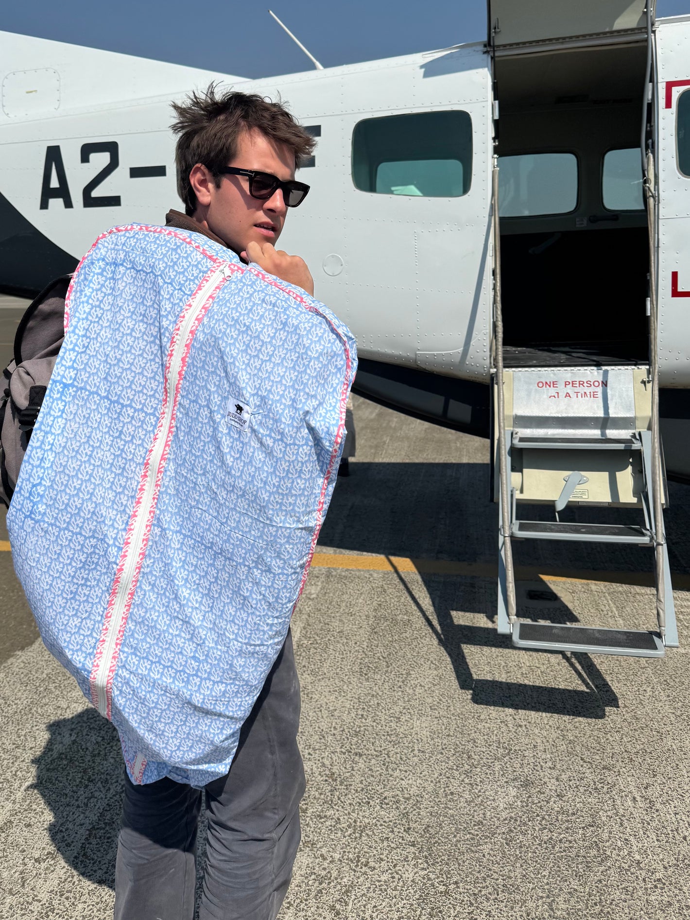 Man carrying a large blue and white patterned bag near an airplane