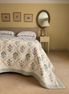 A quilted cream-colored bedspread with a green and pink floral pattern, styled on a bed in a warm, neutral-toned bedroom.