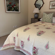 A cream quilted bedspread with pink and green floral patterns and a matching patterned pillow, styled in a bedroom setting.