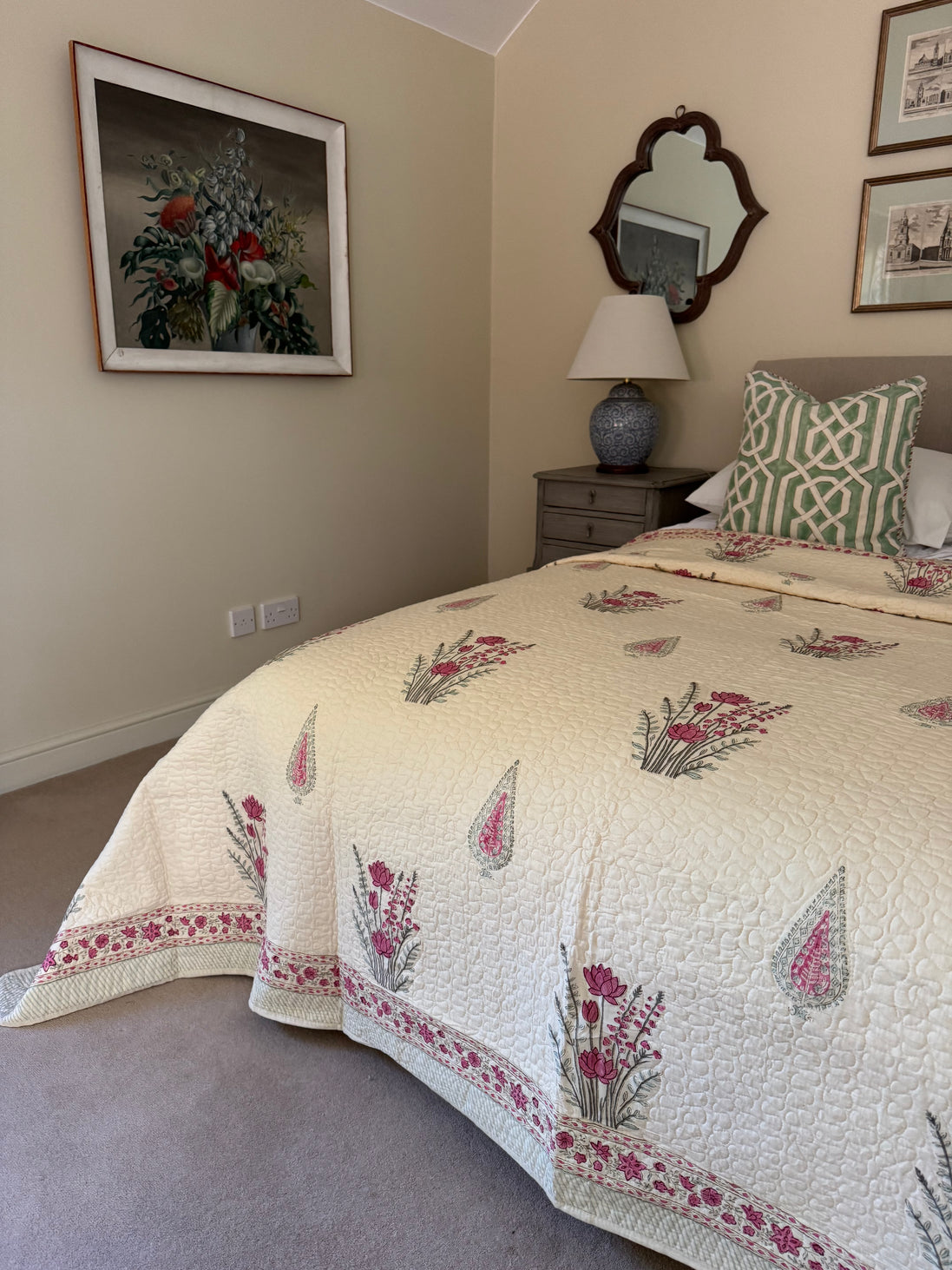 A cream quilted bedspread with pink and green floral patterns and a matching patterned pillow, styled in a bedroom setting.