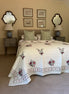 A cream-colored quilted bedspread with red and green floral embroidery and a patterned border, styled on a bed with matching green and white patterned pillows in a bedroom setting.