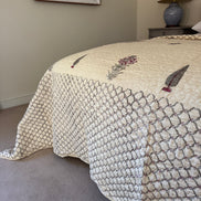 A cream quilted bedspread with a geometric pattern and embroidered floral details, styled on a bed in a bedroom setting.