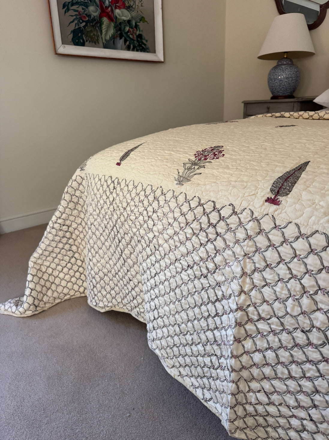 A cream quilted bedspread with a geometric pattern and embroidered floral details, styled on a bed in a bedroom setting.